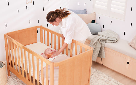 A mother leans over her baby who lies ready for sleep on her beautiful Koala mattress, which does not require a cot mattress protector