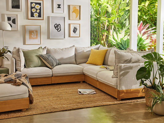 Beige sectional sofa with assorted cushions in a living room. Gallery wall, rug, and indoor plants complement natural light from large window.