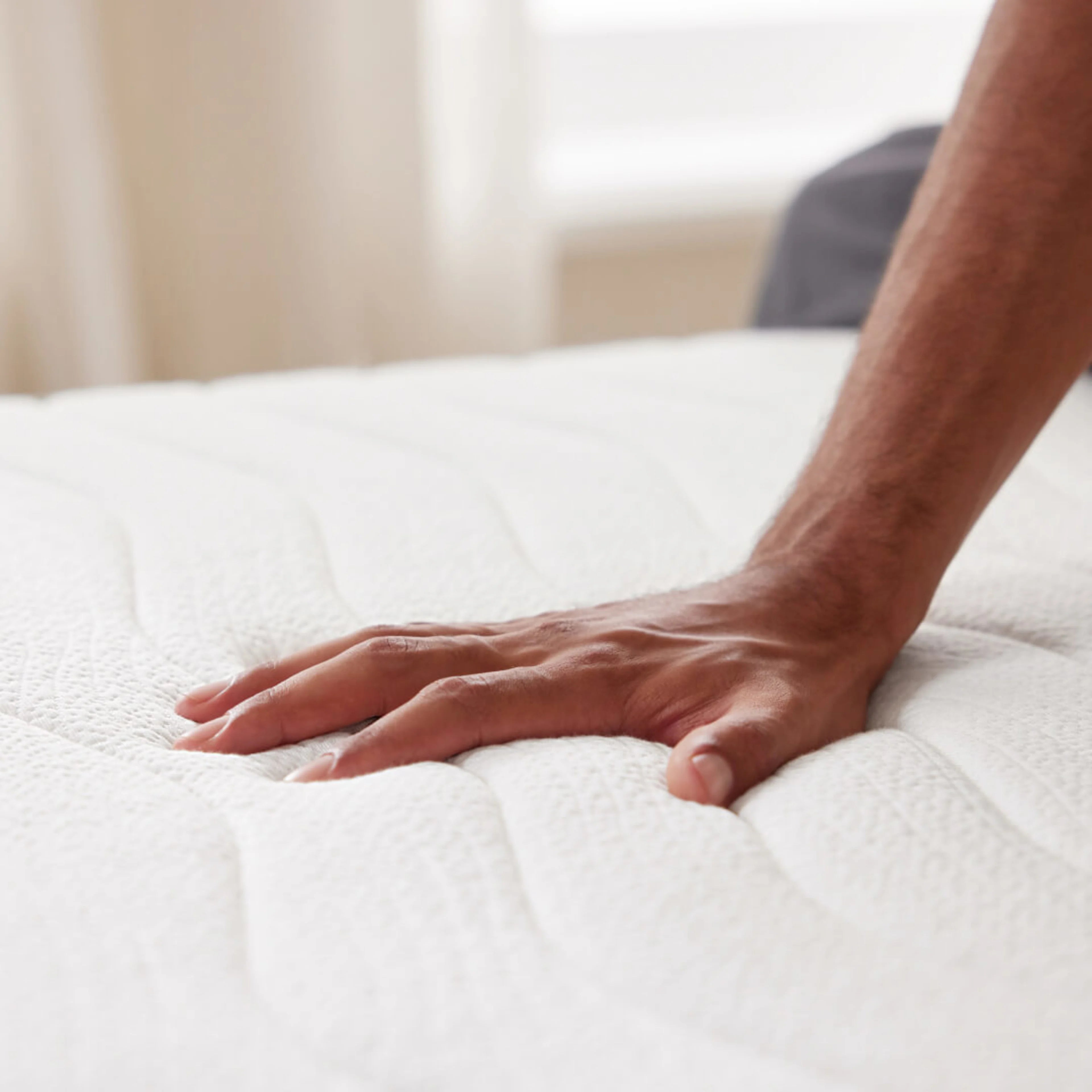 A hand pressing down on a white mattress surface, showcasing its plush texture.