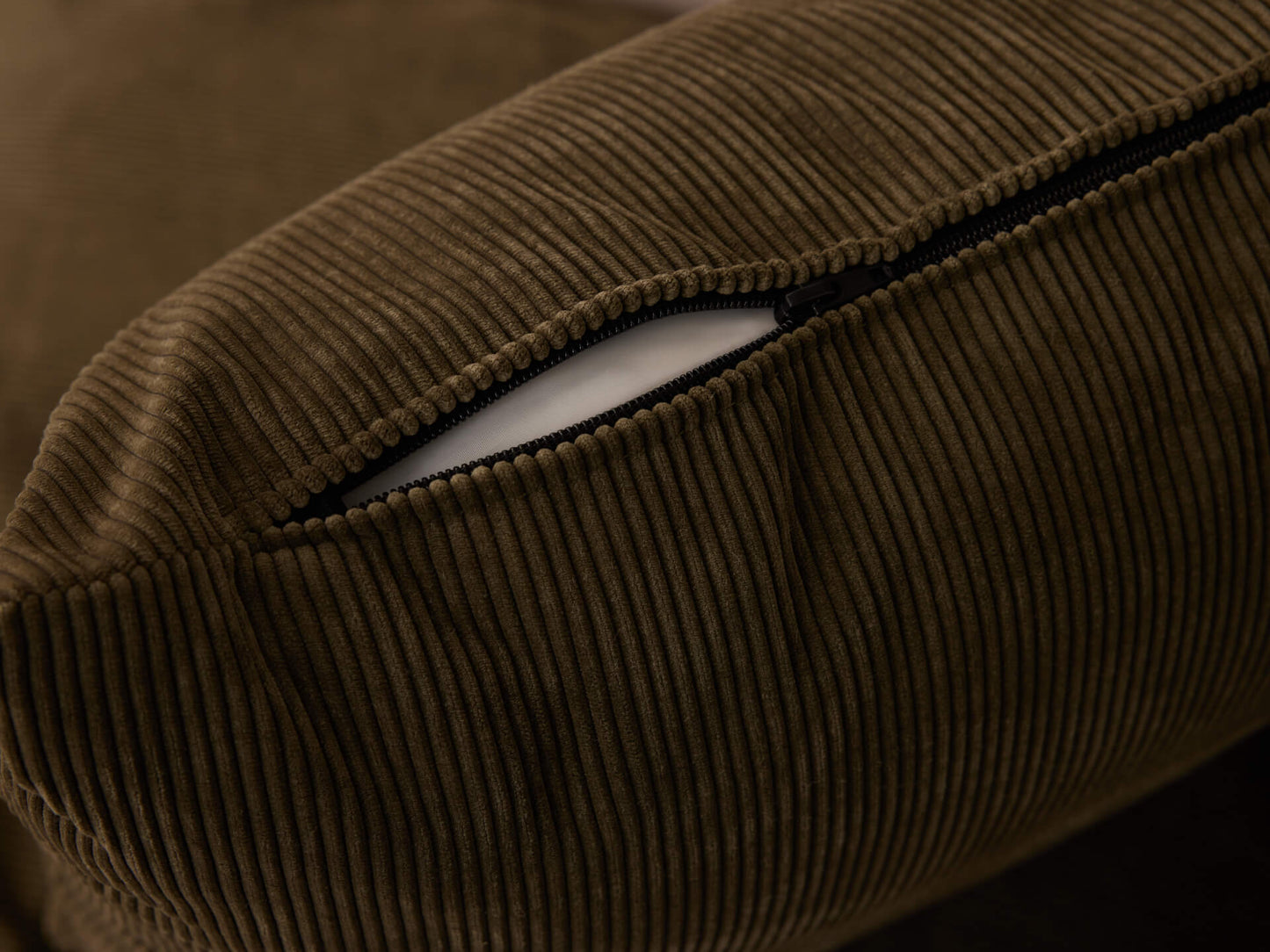 Brown corduroy cushion with visible black zipper on the side, revealing white inner lining. Close-up detail of fabric texture and design.