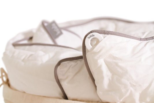 Close-up of a white baby bassinet with grey trim, showing padded edges and a button detail.