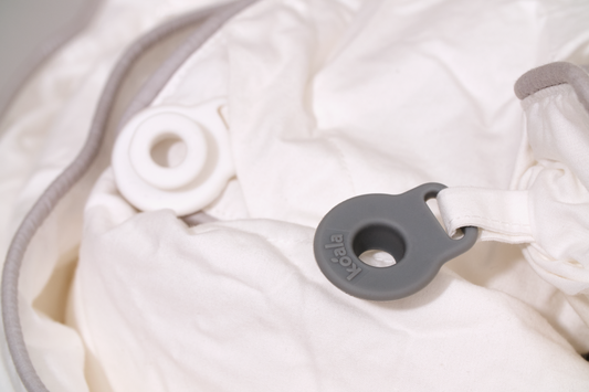 White fabric with grey trim and two circular rings, one grey and marked with text, lying on the material.