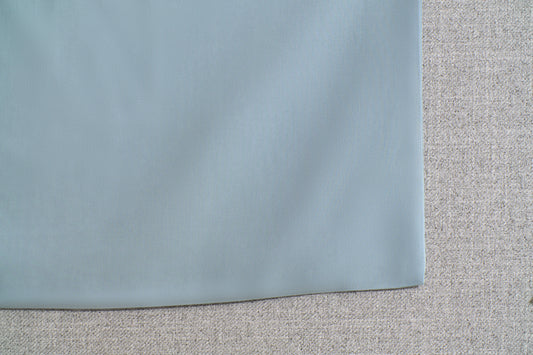 Close-up of a light grey fabric overlaid on a textured beige surface, possibly showing upholstery or textile material.
