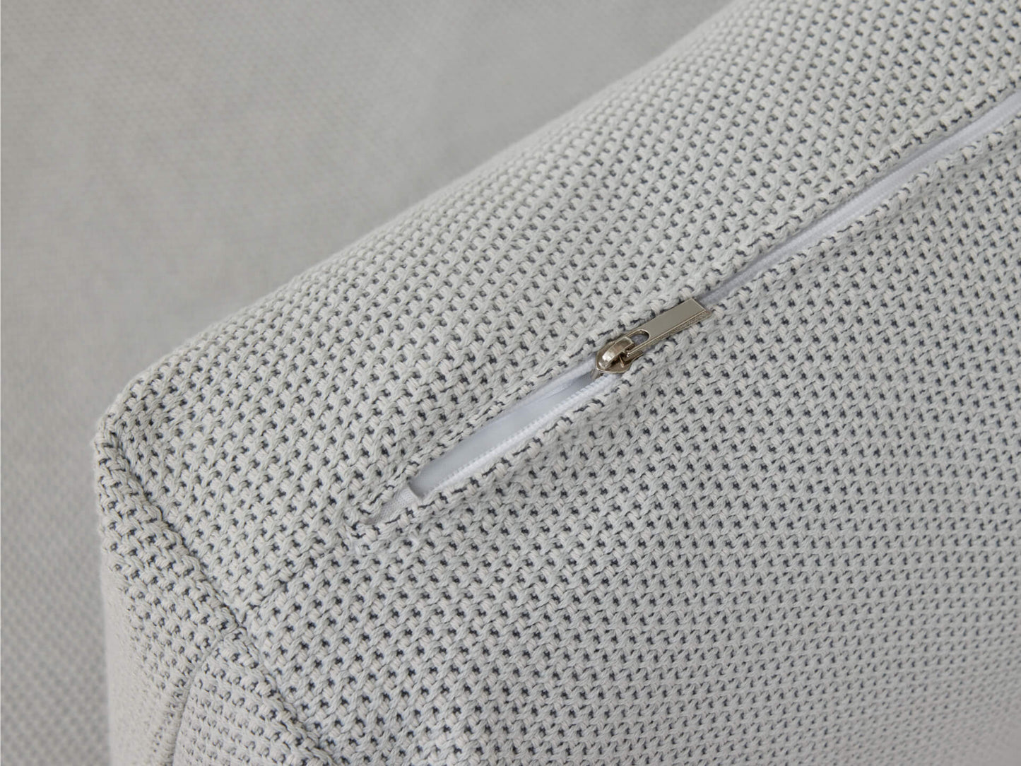 Close-up of a textured light grey cushion with a visible white zipper on the side, showcasing fabric detail and stitching.