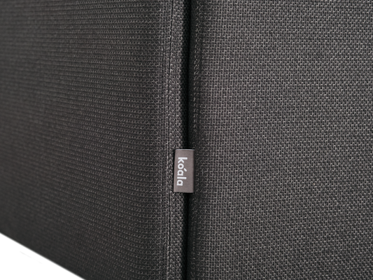 Close-up of dark grey textured fabric with a small "koala" tag, likely part of a sofa or cushion.