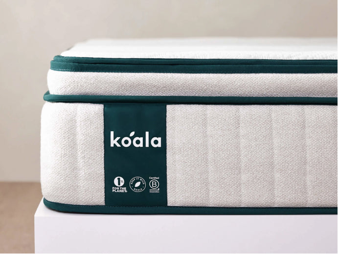 Close-up of a grey mattress with green trim, featuring a "koala" label, resting on a white surface.