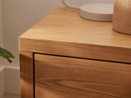 Close-up of a light brown wooden cabinet corner, showcasing wood grain texture, with a round grey base and beige decorative item on top.