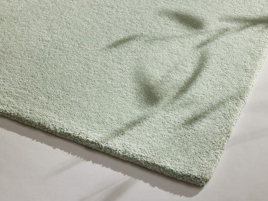 Light green textured mat on a white floor, with soft shadows resembling leaves cast over it.