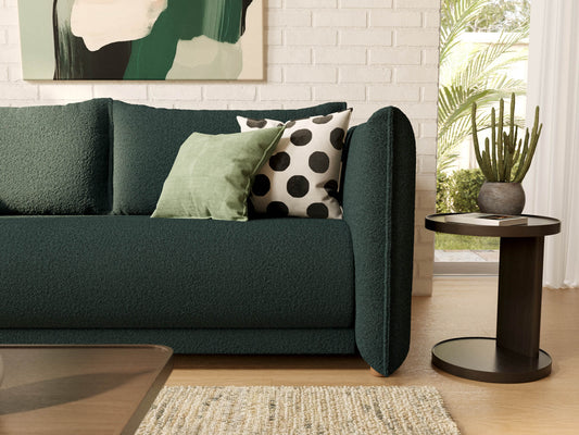 Dark green sofa with textured fabric, topped with green and polka dot cushions. Nearby, a round dark table with a cactus and a rug on the floor.