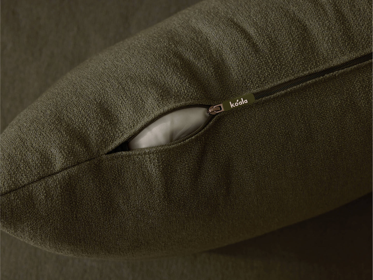 Olive green cushion with open zip revealing white filling on a matching upholstered surface.