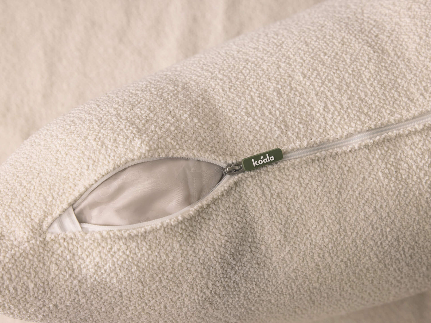 Close-up of a white textured cushion with an open zipper, revealing its inner lining. A green tag is visible near the zipper.