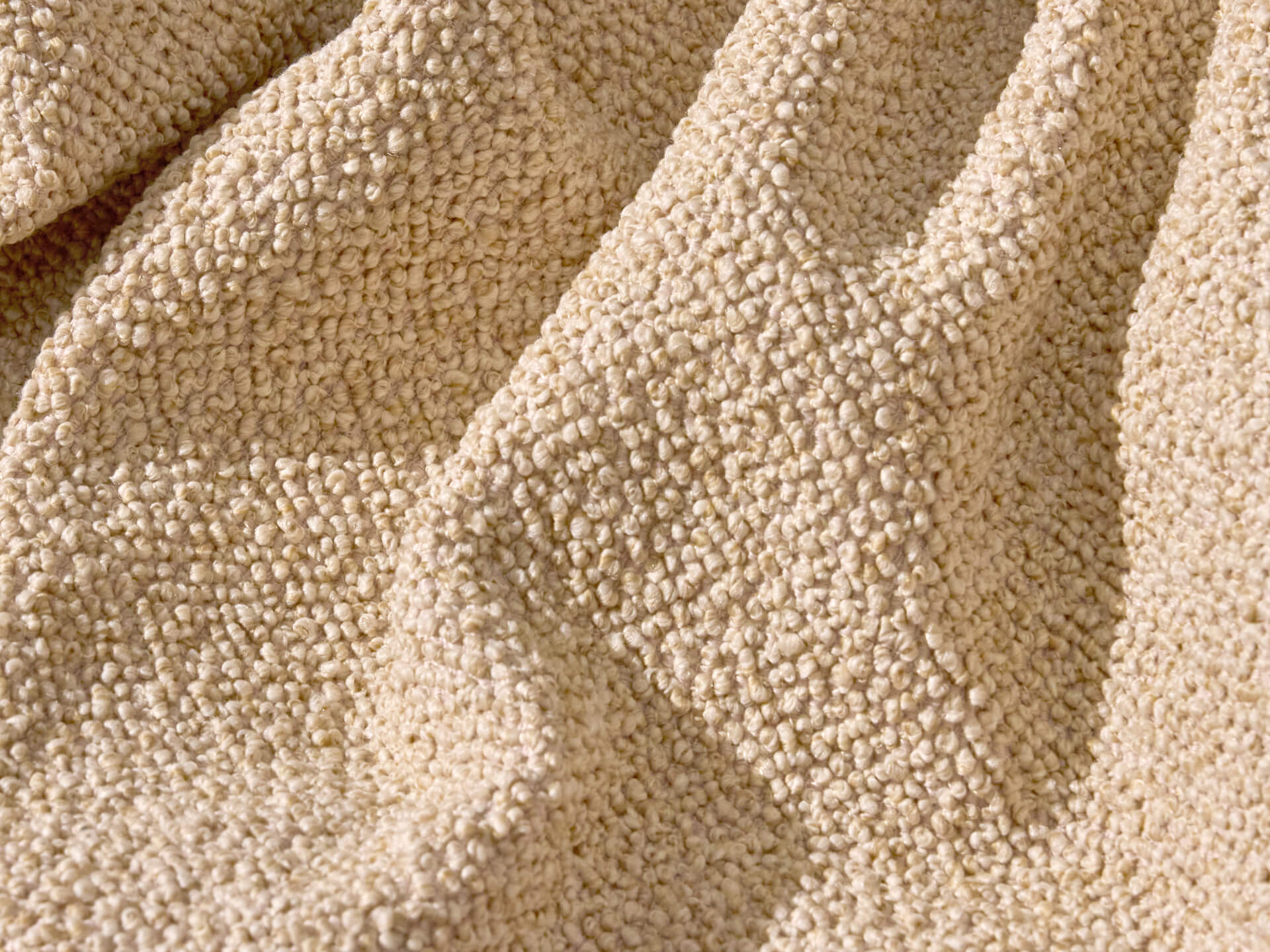 Textured beige boucle fabric with soft folds, showcasing its intricate weave and cosy appearance. Perfect for upholstery or home decor.
