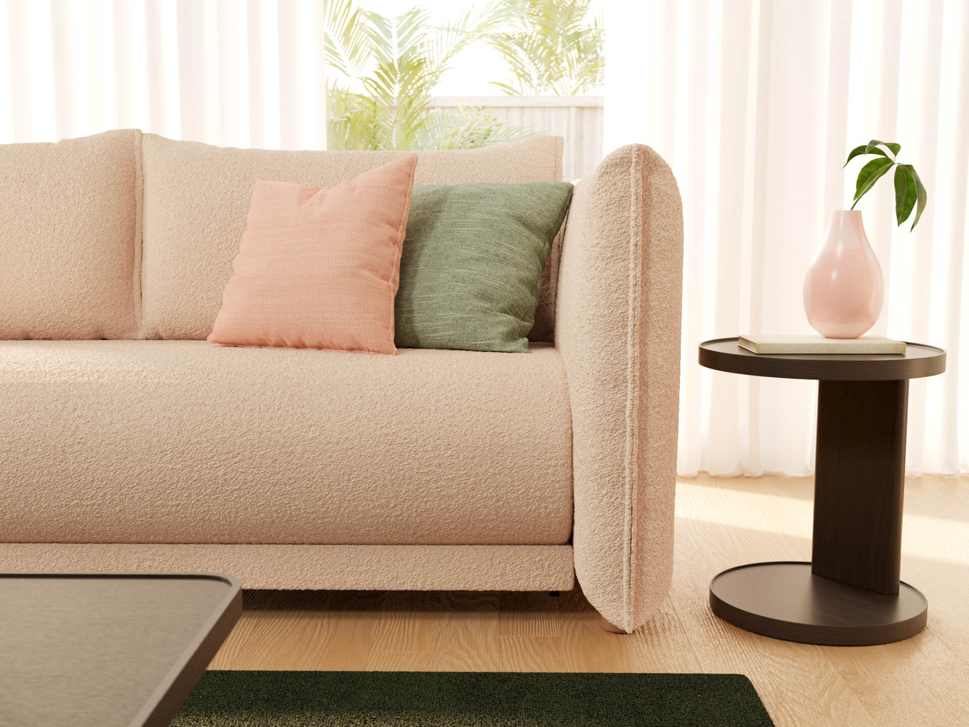 Cream sofa with peach and green cushions, beside a dark wood side table with a pink vase. Light curtains and green plants in the background.