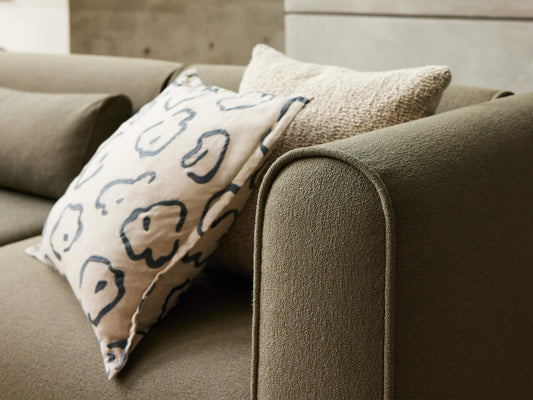 Olive green sofa with rounded armrests, featuring two cushions: one textured beige and one with a white and black abstract pattern.