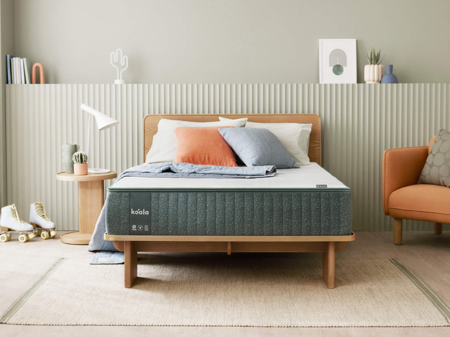 Bedroom with a wooden bed frame and dark grey mattress. Orange and grey cushions, wooden side table, skates, and light grey wall accents.