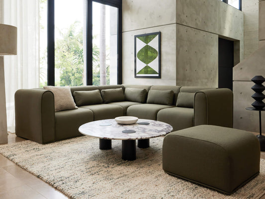 Olive green modular couch in modern living room with marble coffee table, large windows, abstract art, and a textured beige rug.