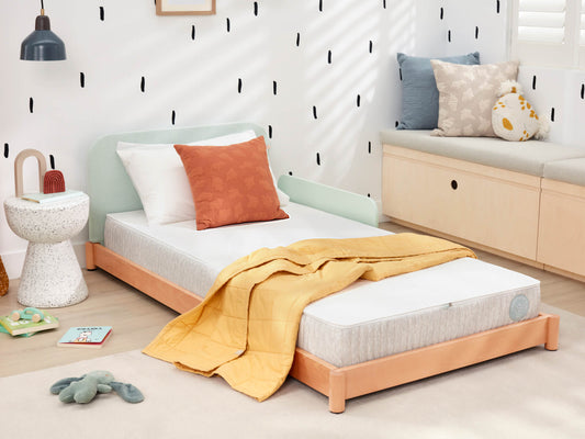 Children’s bedroom with a single bed featuring a light grey mattress and a wooden frame, adorned with a yellow quilt and orange pillow.