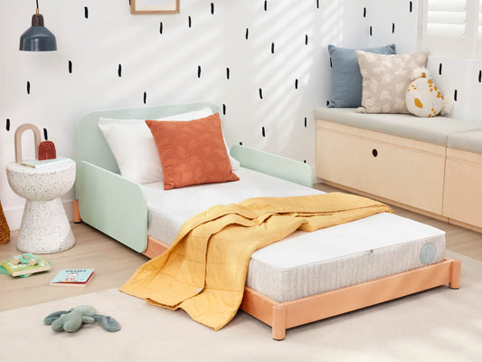 Children's bedroom with a single bed, mint green headboard, orange quilt, and a white side table. Cushions on a light wood bench.