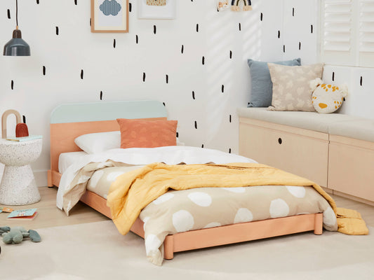 Children's bedroom with a light wood single bed, polka dot bedding, yellow throw, and colourful cushions. Minimalist decor with playful accents.