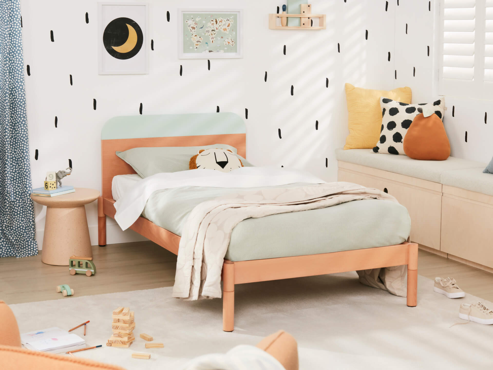 Stylish kids' bedroom with a light wood bed, mint green bedding, and polka dot cushions. Black and white wall pattern enhances modern decor.