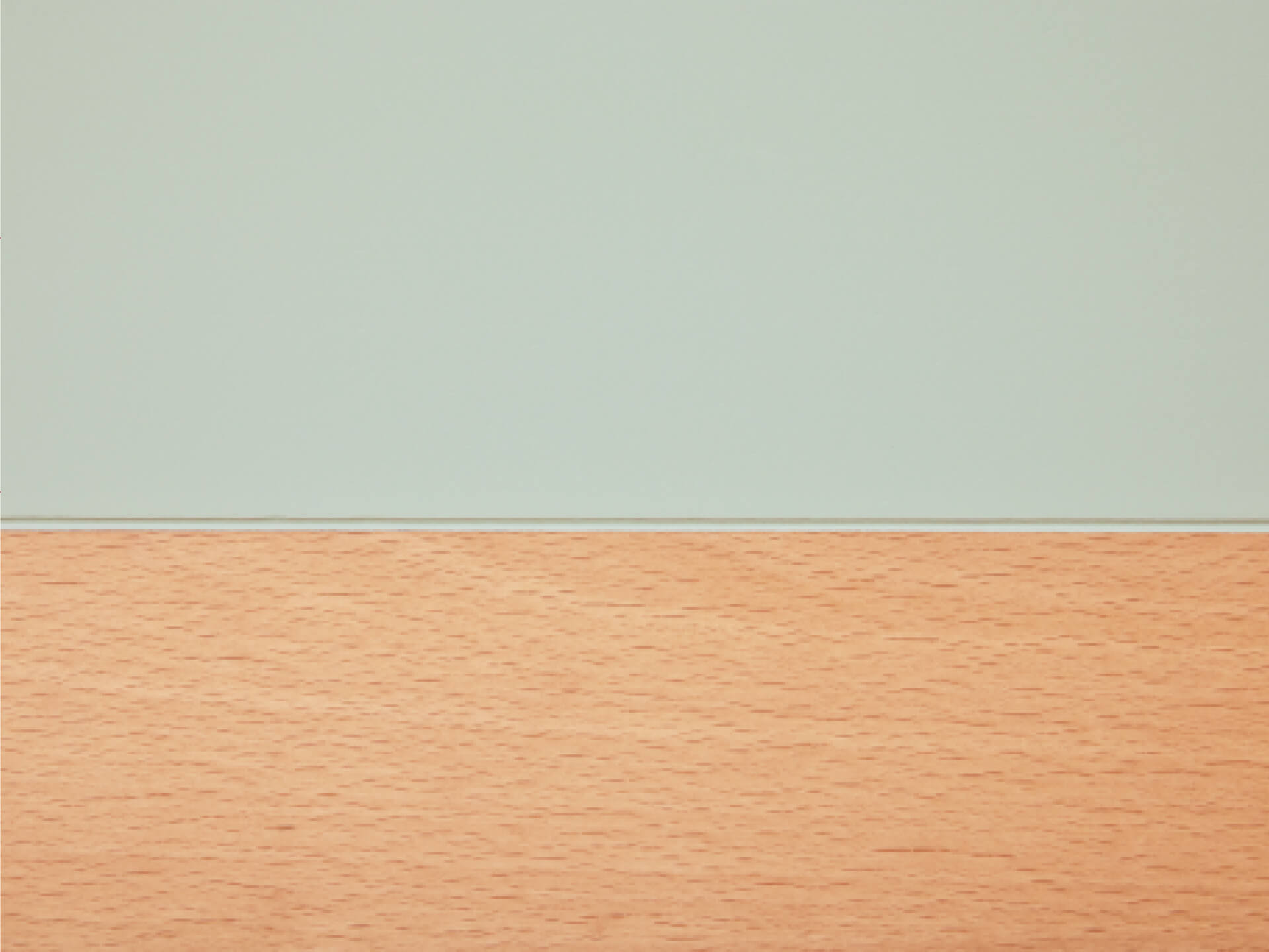 Light brown laminate wood surface below a pale green wall, showcasing a simple and modern interior design theme.