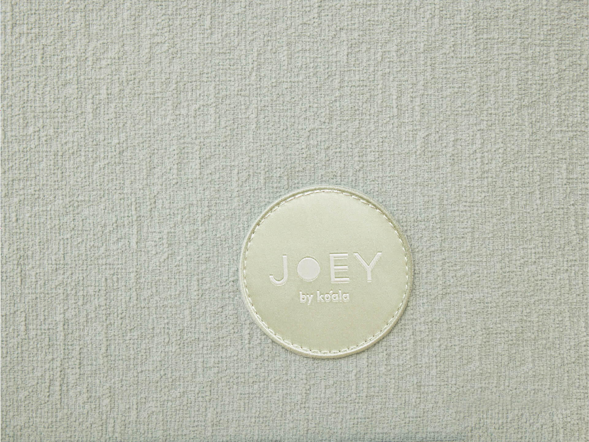 Light grey textured fabric with a circular patch in the centre, reading "JOEY by Koala" in white text. Ideal for furniture or upholstery.