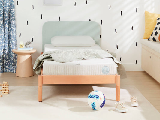 Child's bedroom with a single bed, light wood frame, and pale green headboard. Ball, shoes, and small table nearby on a light floor.
