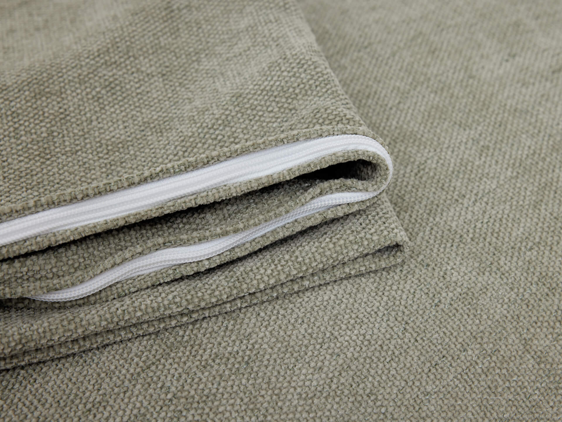 Close-up of a folded light grey fabric with a visible white zipper. Perfect for upholstery or cushion covers. Textured and durable material.