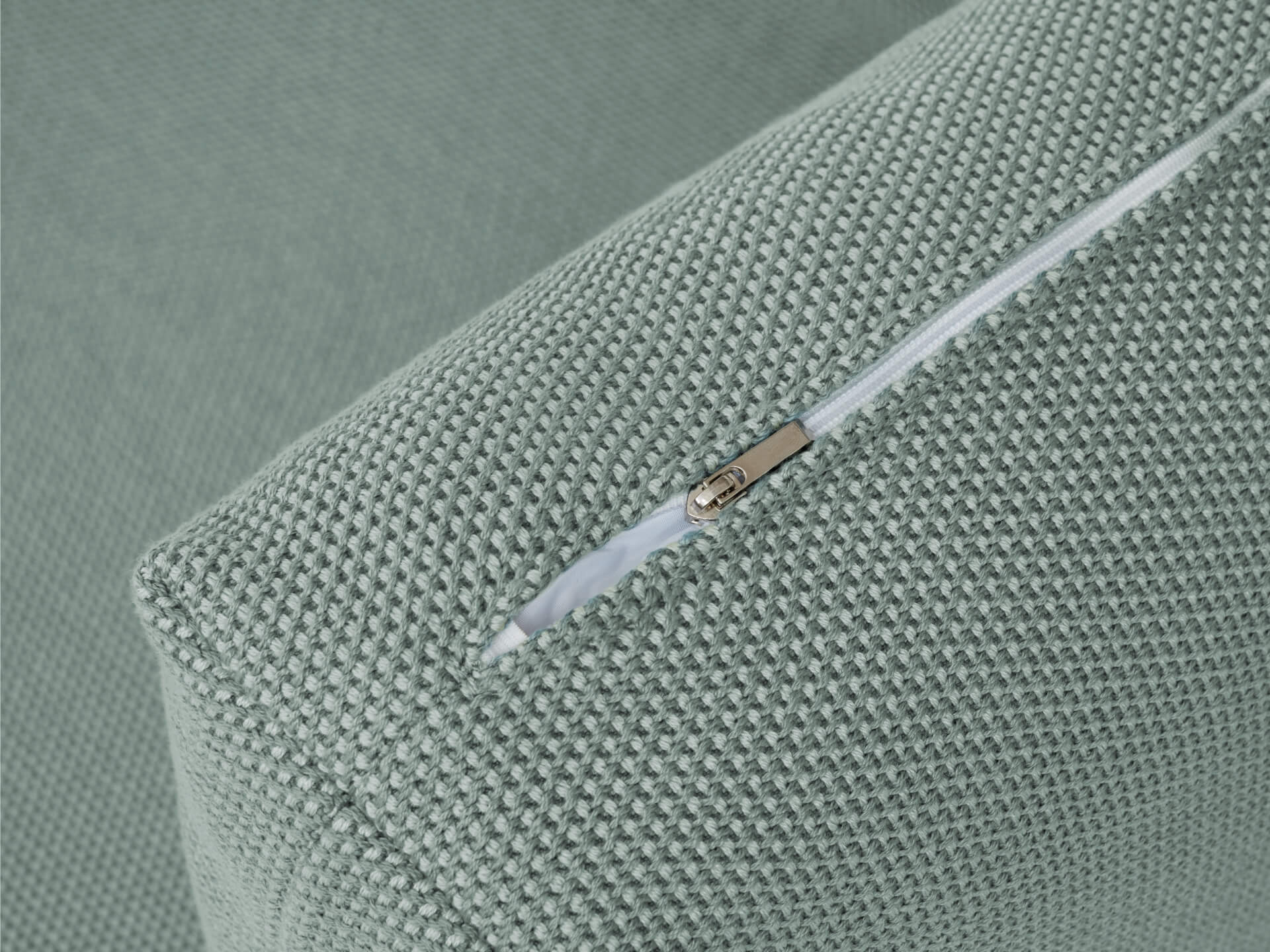 Close-up of textured green fabric cushion corner with a white zipper. Ideal for upholstery, sofa, couch, or cushion design detail.