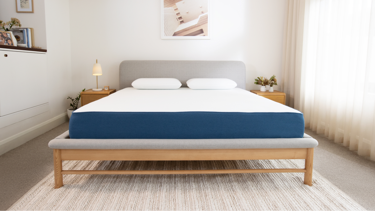 Modern bedroom with a wooden bed frame, grey fabric headboard, and blue-striped mattress. Two white pillows, bedside tables, and lamps.