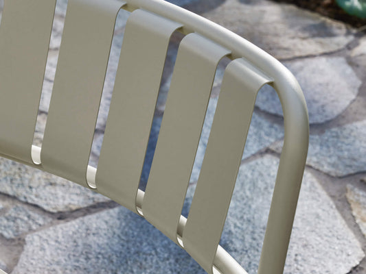 Close-up of a beige metal chair's slatted backrest on a stone patio.