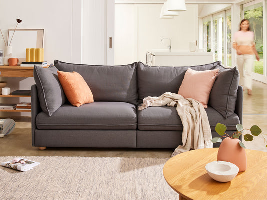 Dark grey sofa with peach cushions and a beige throw in a stylish living room. Wooden coffee table and shelf with decor items in the background.