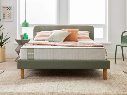 Bedroom with a green upholstered bed, light grey mattress, peach and grey pillows, striped bedding, and a green chair. Decor includes plants and wall art.