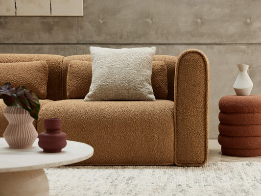 Brown textured sofa with a light grey cushion, alongside a round white coffee table and stacked cylindrical side table, in a modern setting.
