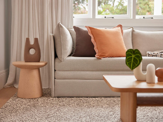 Stylish living room with a beige sofa adorned with brown and orange cushions, a wooden coffee table with decor, and a textured beige rug.