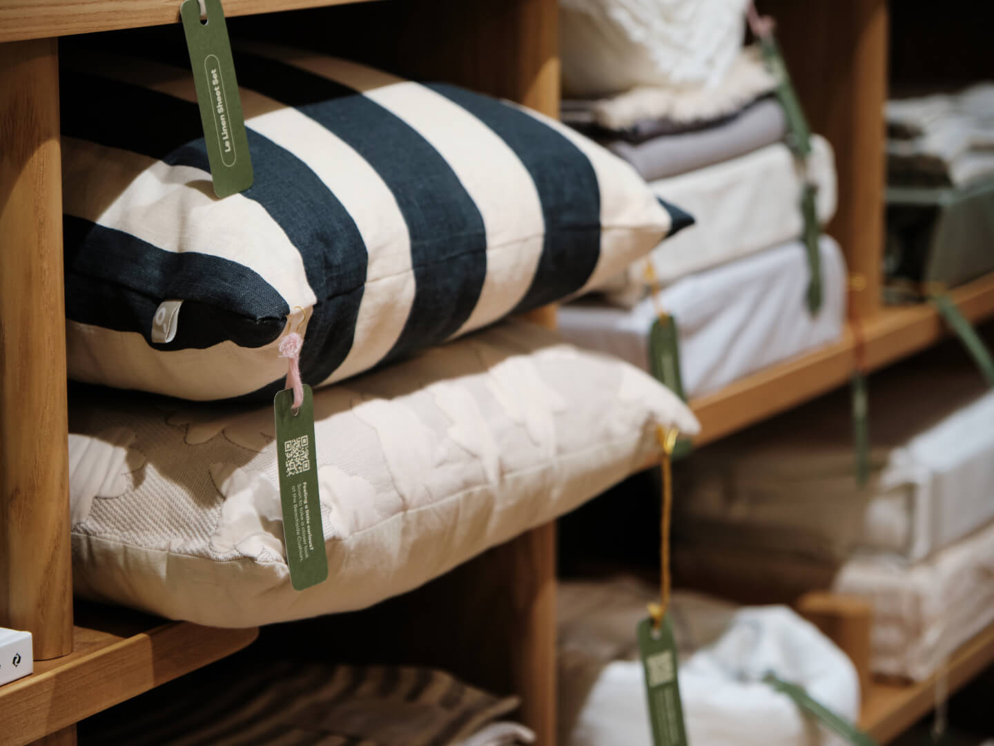 Shelves displaying cushions, including a blue and white striped cushion and beige cushions, each with hanging green price tags.