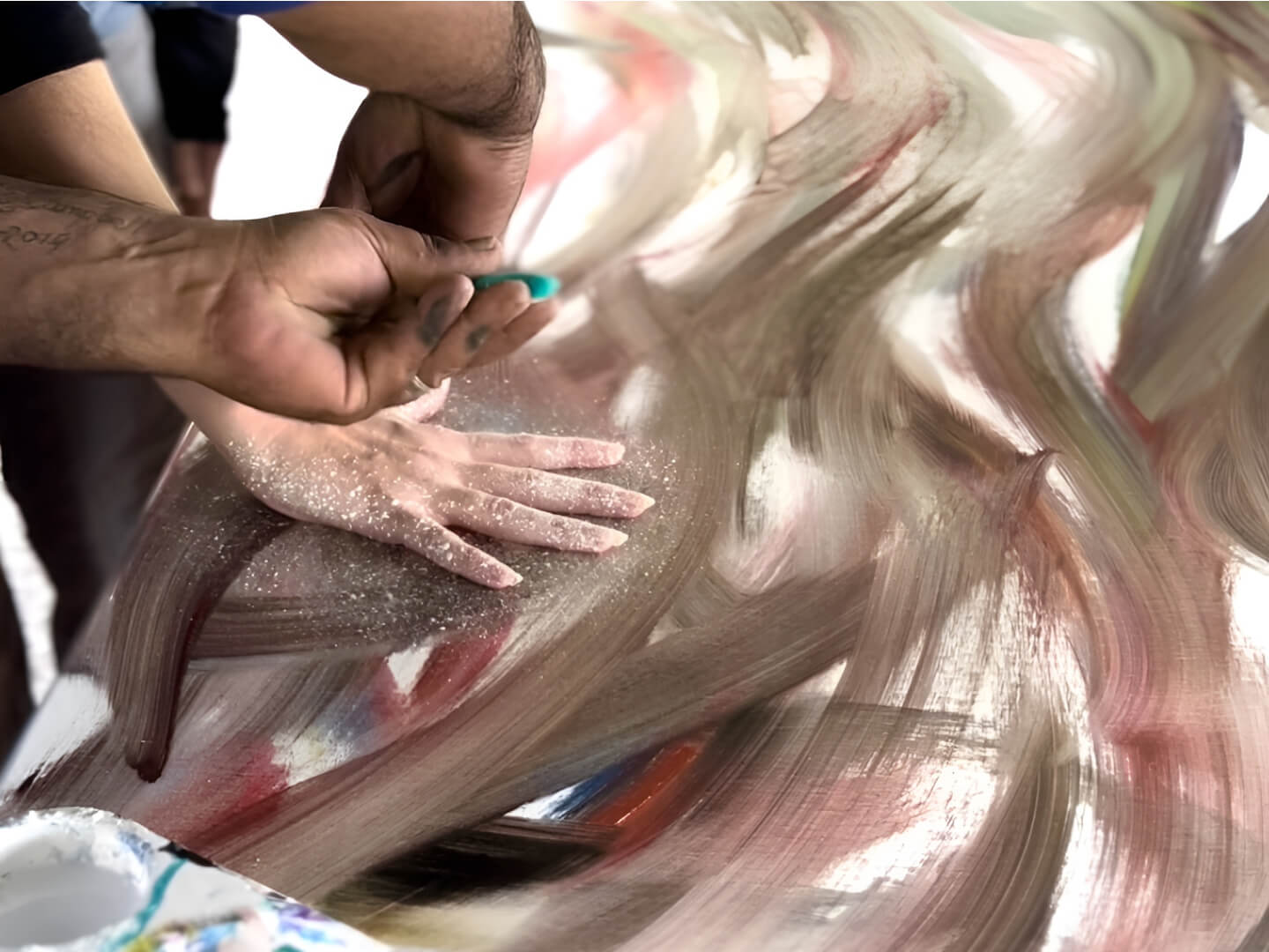 Hands spreading glitter over a swirling abstract painting with beige, brown, and red tones.