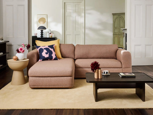 Beige sectional sofa with colourful cushions on a light rug. Brown coffee table with decor items nearby; side table with decorative pieces. Elegant living room.