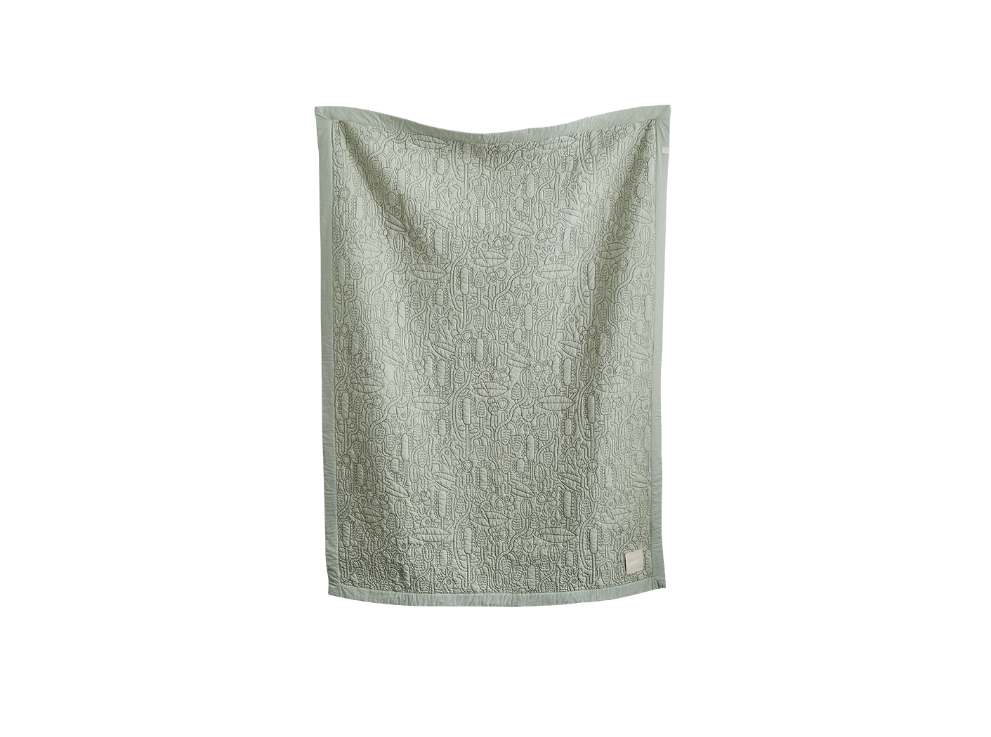 Light green textured quilt hanging, displaying intricate patterns. Fabric label on the bottom right corner.