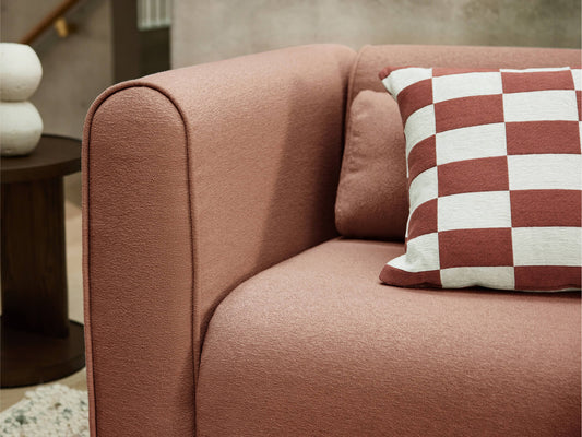 Close-up of a dusty pink sofa with a red and white checkered cushion. Dark wood side table and light-coloured wall in the background.