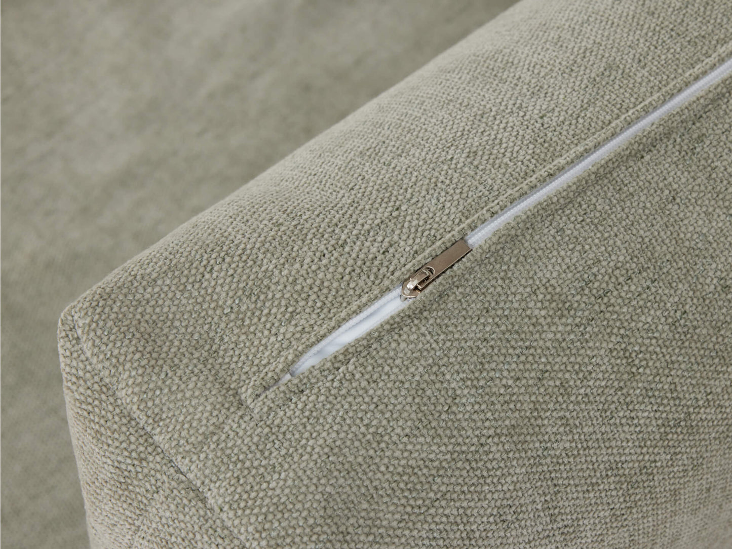 Close-up of a green fabric couch cushion with a visible white zip on the seam. The texture looks slightly coarse.