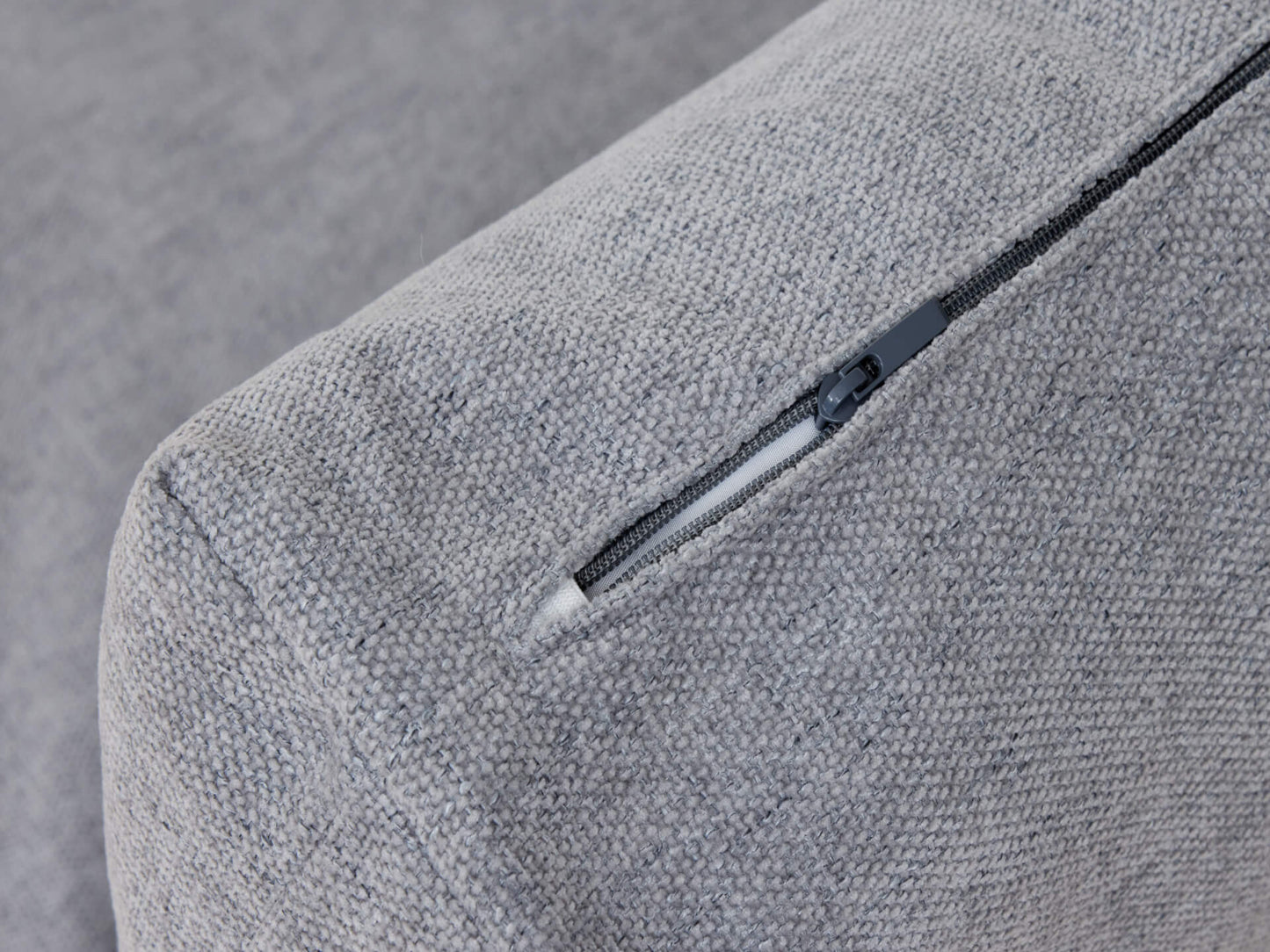Close-up of a light grey textured sofa cushion with a partially open black zip on the edge.