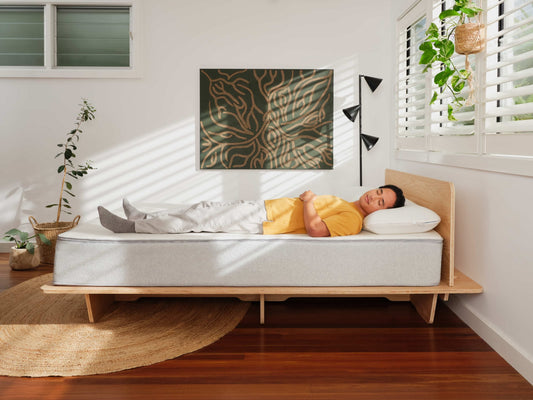 Man in yellow t-shirt lying down on a mattress trying to figure out if it’s the best mattress for him