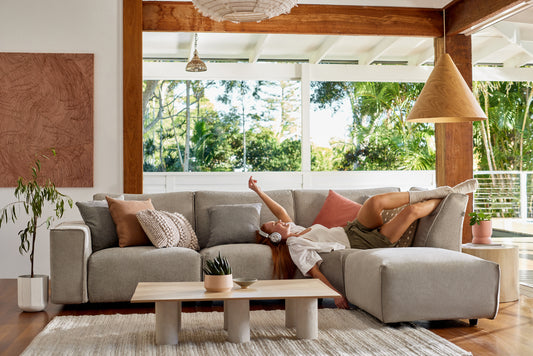 A young woman lies on her Koala sofa and listens to music in a large open lounge room