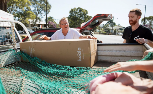 Two men standing over ute with Koala mattress box in tray