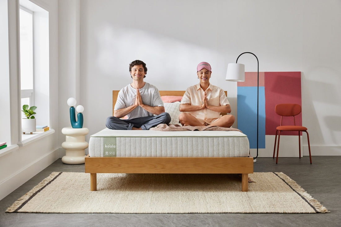 A young, smiling couple relax in a meditation pose on their newly arrived Koala SE Mattress and Balmain bed base