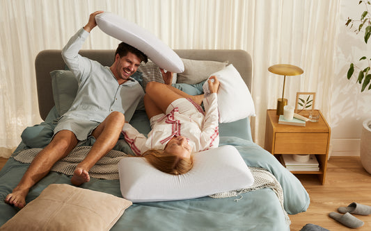 A playful couple laugh in bed after discovering the best pillow for side sleepers