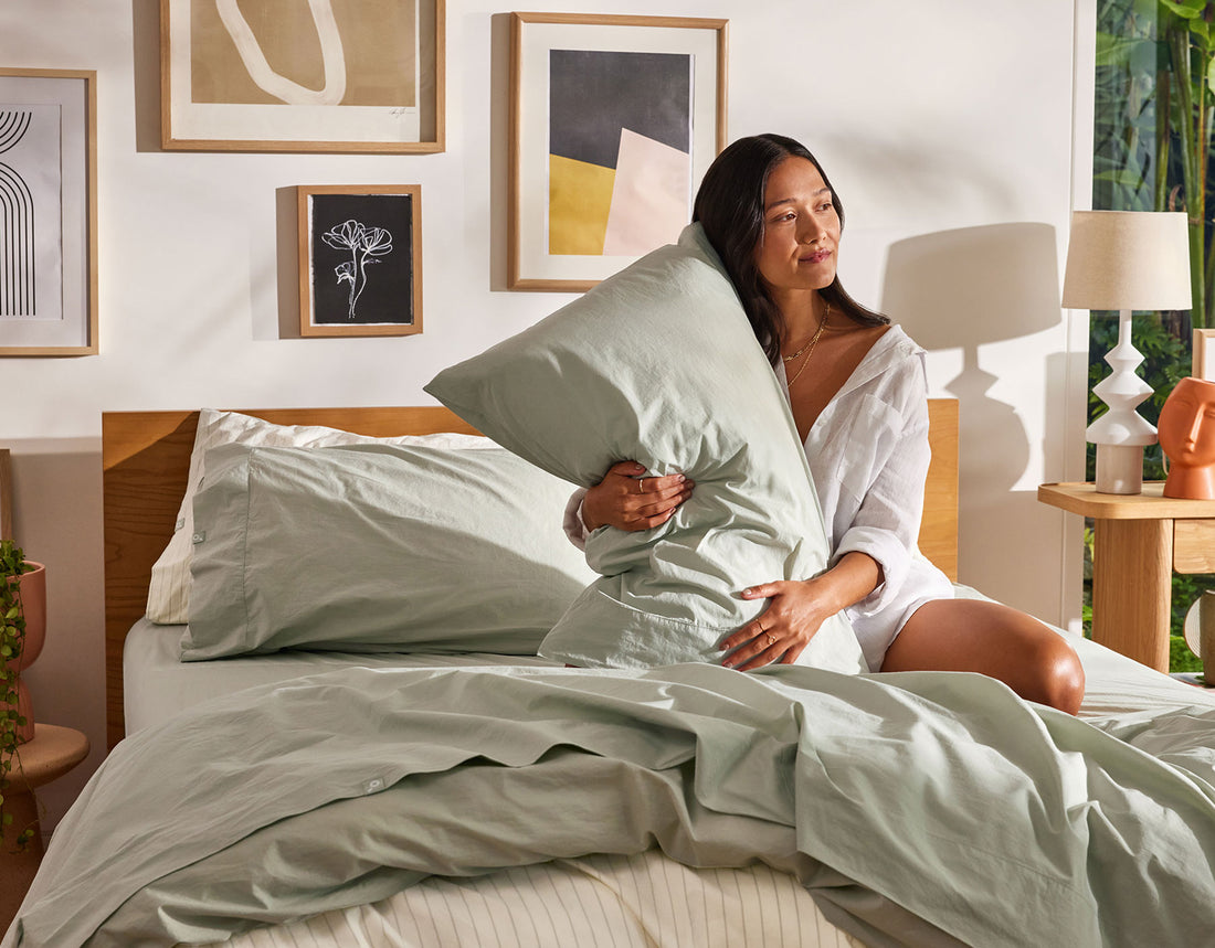 A well-rested woman sits on her unmade bed after discovering Koala has some of the best sheets in Australia