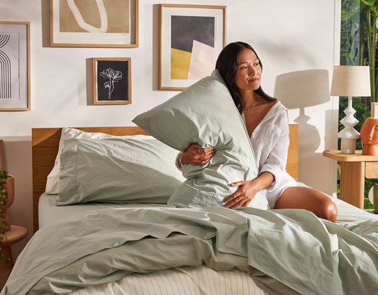 A well-rested woman sits on her unmade bed after discovering Koala has some of the best sheets in Australia