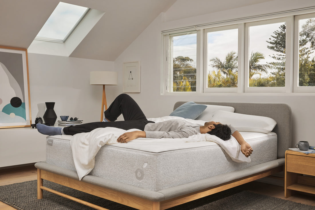 A man lies on a Koala mattress on a Koala bed frame in a bright, airy bedroom.